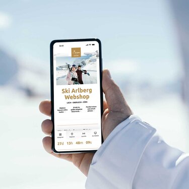 Person hält Handy mit geöffneter Ski Arlberg Webshop-Seite im Schnee.