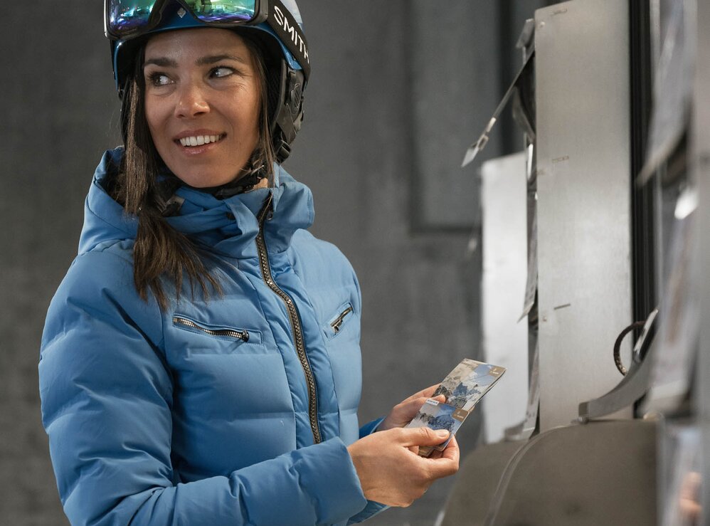 Frau in Skijacke und Helm kauft Skipässe am Ticketschalter.