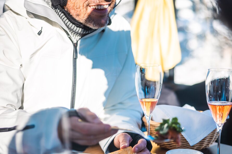 Mann in Skiausrüstung genießt Gourmet-Essen und Champagner in einer Gondel.
