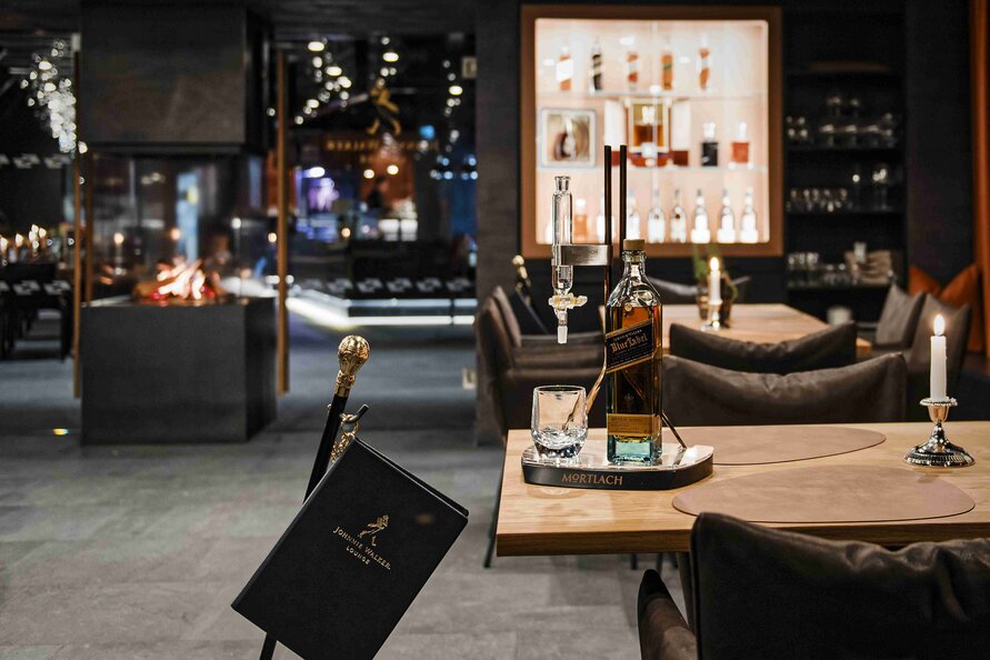 Ein stilvoller Tisch im Schlegelkopf Restaurant mit einer Flasche Mortlach, Glas und Kerze, getaucht in gemütliches Ambiente.