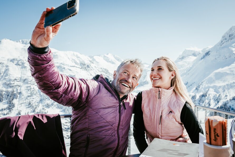 Paar macht ein Selfie auf der Terrasse des Schlegelkopf Restaurants mit atemberaubenden Winterpanorama