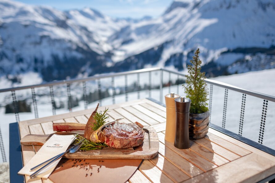Steak mit Beilage auf einem Tisch im Schlegelkopf Restaurant vor schneebedeckter Bergkulisse.
