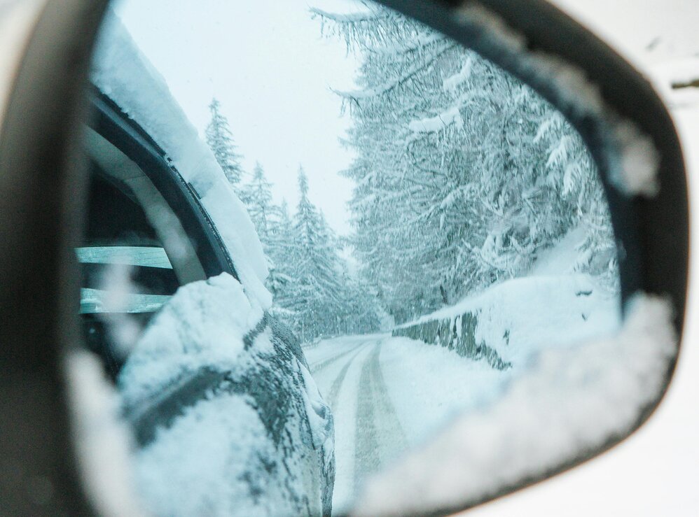 Autospiegel zeigt schneebedeckte Straße und Bäume im Winter.