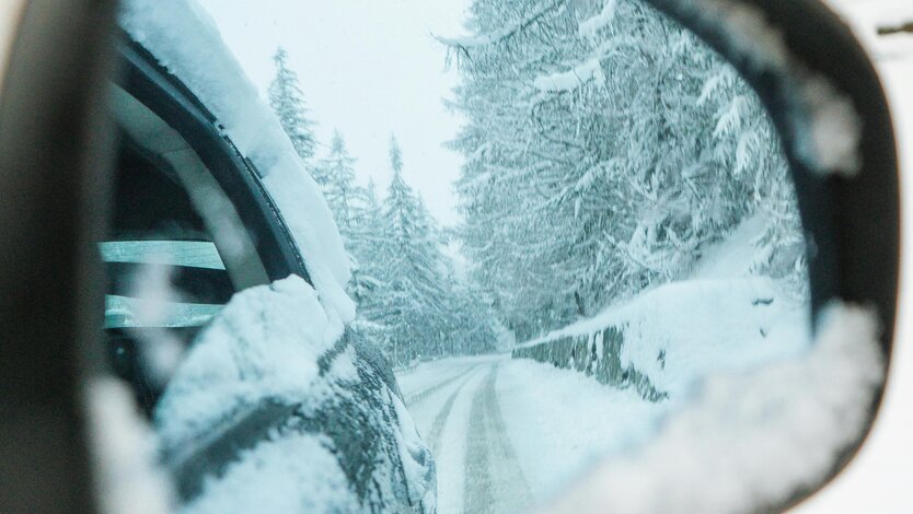 Autospiegel zeigt schneebedeckte Straße und Bäume im Winter.