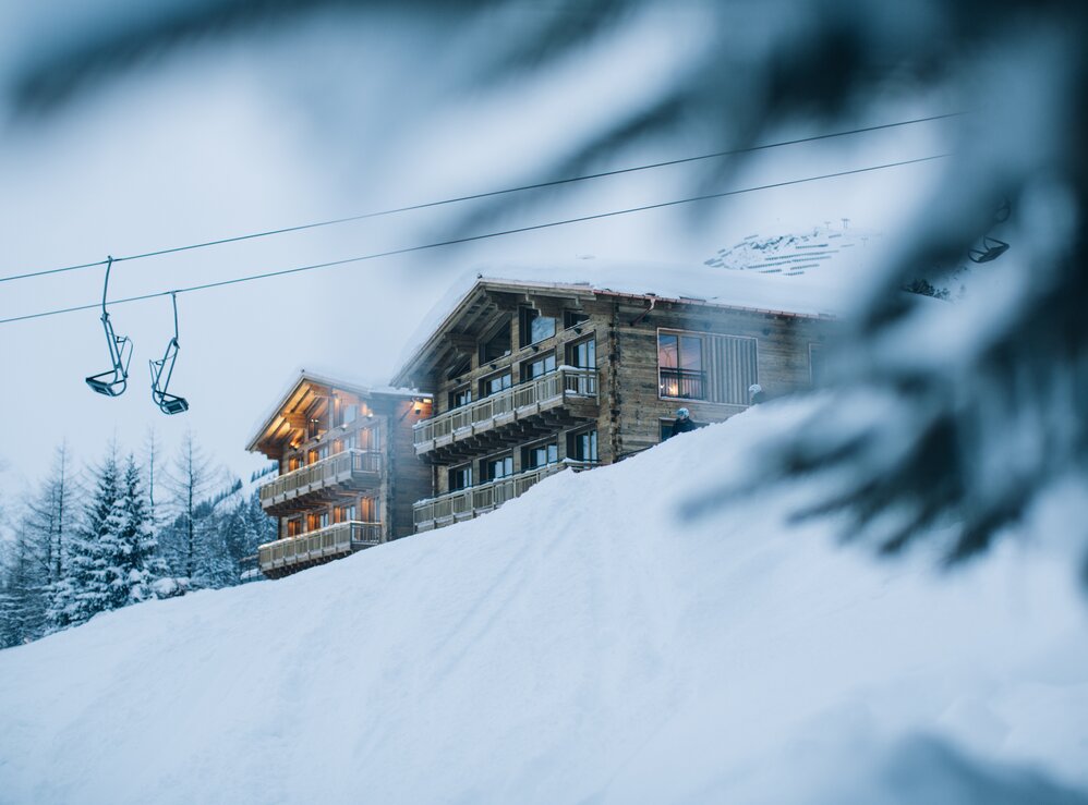 Eine Berghütte aus Holz und ein Sessellift in einer schneebedeckten Berglandschaft.