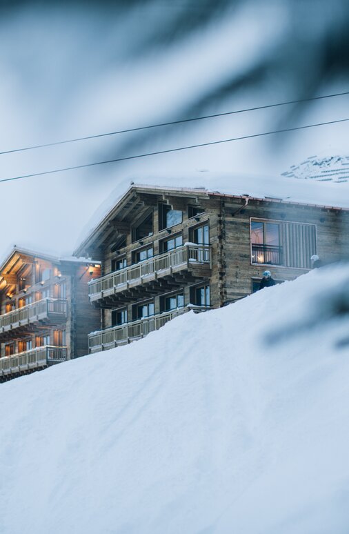 Eine Berghütte aus Holz und ein Sessellift in einer schneebedeckten Berglandschaft.