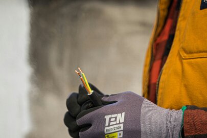 Person mit einer gelben Jacke hält Kabeln in den Händen und trägt dabei Schutzhandschuhe.