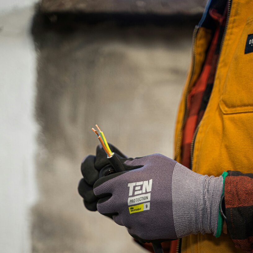 Person mit einer gelben Jacke hält Kabeln in den Händen und trägt dabei Schutzhandschuhe.
