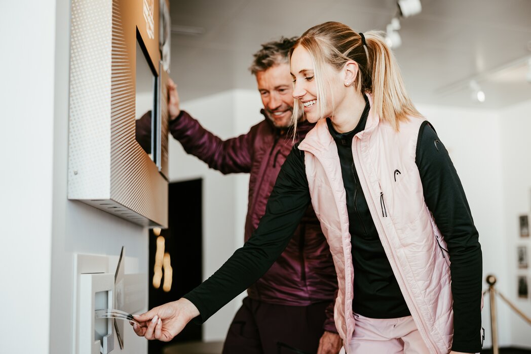Ein Paar nutzt einen Ticketautomaten beim 'Run of Fame'. Sie sind lächelnd an einem Schalter beschäftigt.