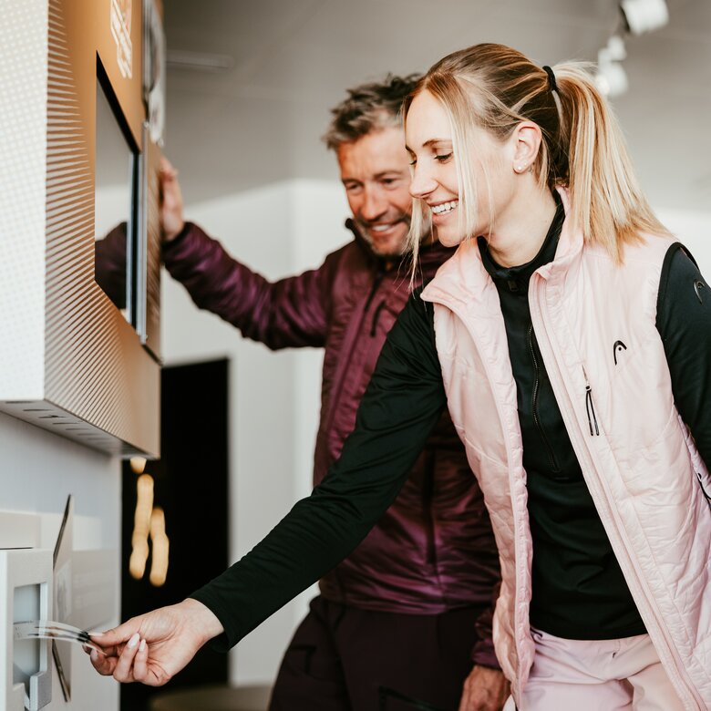 Ein Paar nutzt einen Ticketautomaten beim 'Run of Fame'. Sie sind lächelnd an einem Schalter beschäftigt.