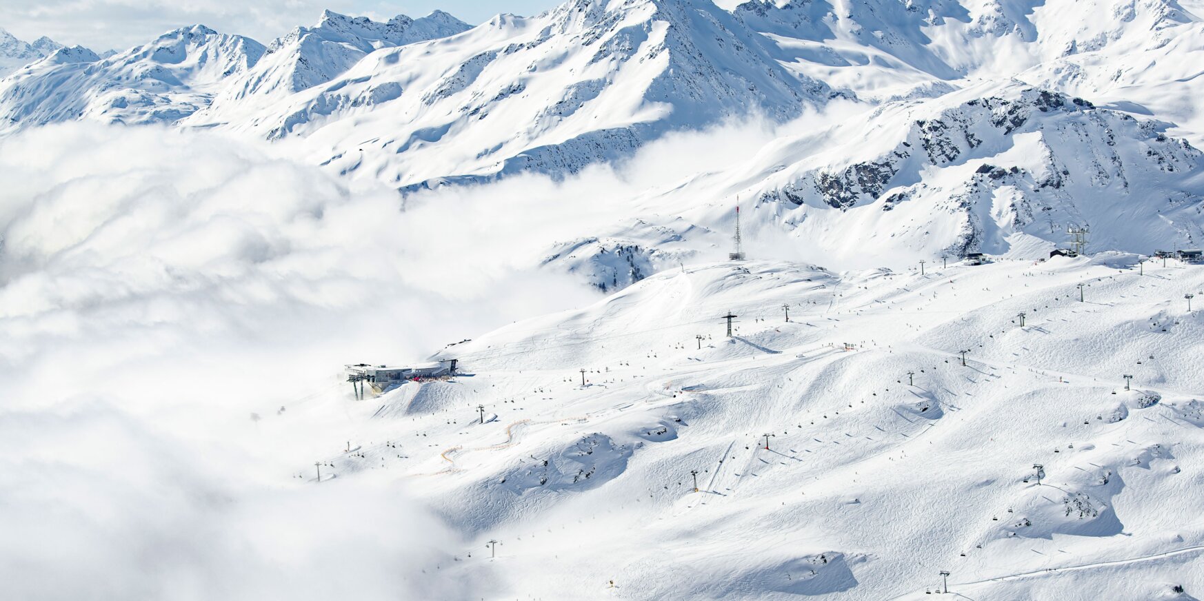 Verschneite Berge und Skipisten im Ski Arlberg bei blauem Himmel.