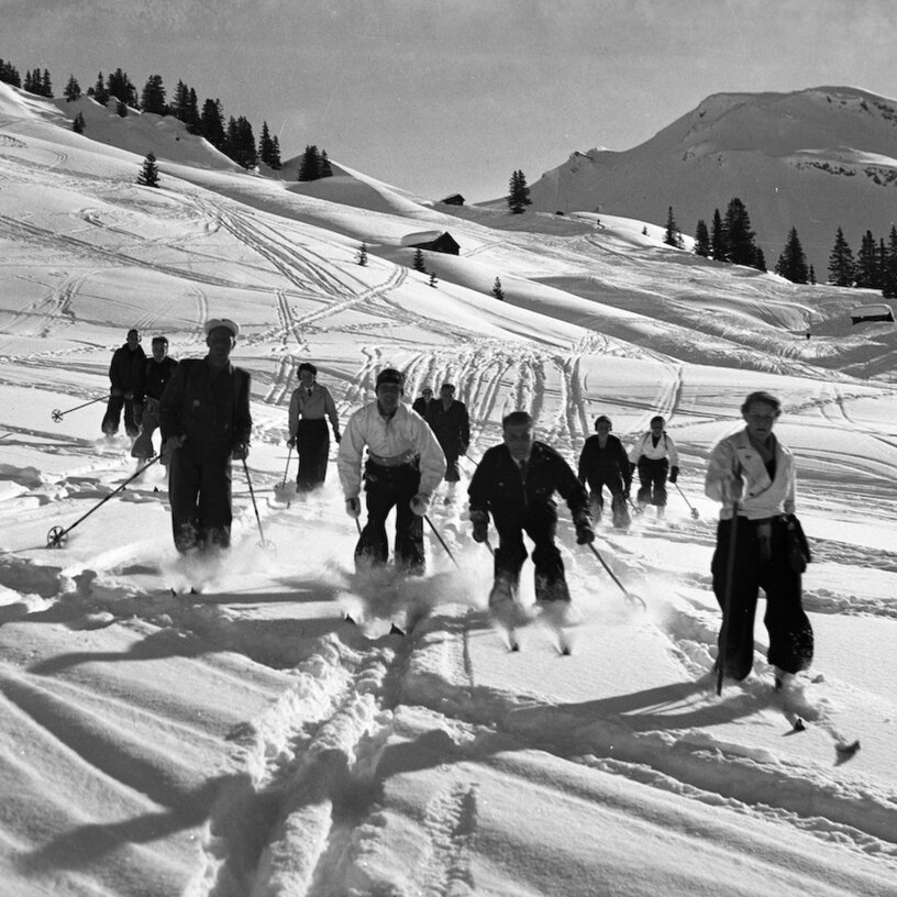 Schwarz-Weiß-Bild einer Gruppe Skifahrer, die durch den Tiefschnee fahren.