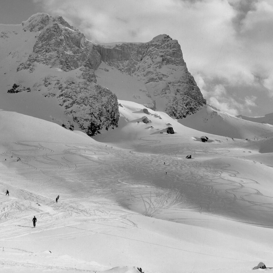 Schwarz-Weiß-Foto: Das Skigebiet Ski Arlberg früher mit Skifahrern und Bergen.