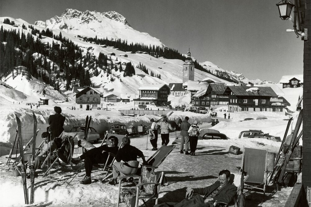 Schwarz-Weiß-Bild: Menschen genießen einen sonnigen Wintertag in Ski Arlberg. Im Hintergrund Berge und Schnee.
