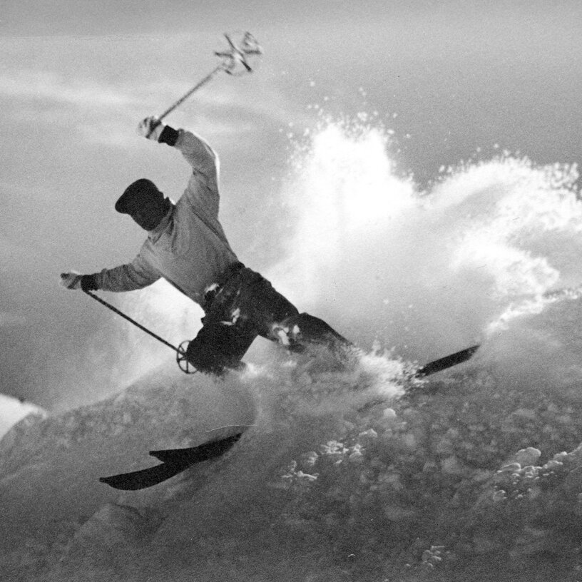 Schwarz-Weiß-Bild: Skifahrer fährt schwungvoll durch frischen Pulverschnee.