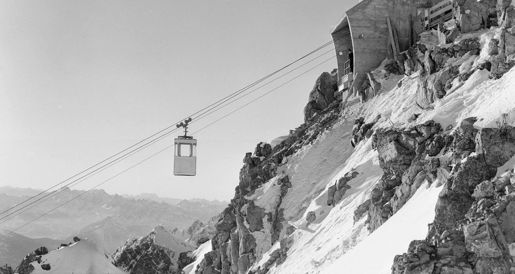 Schwarz-Weiß-Bild: Seilbahn nahe Station auf schneebedecktem Berggipfel.