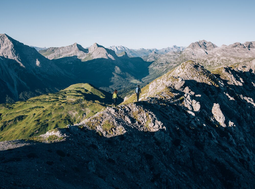 2 Wanderer auf Bergkamm mit weitem Bergpanorama klarer Sicht und blauem Himmel.