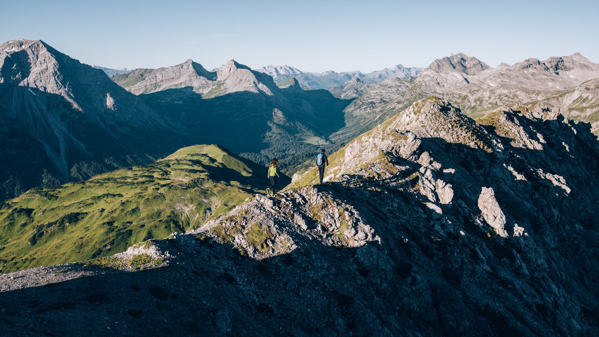 2 Wanderer auf Bergkamm mit weitem Bergpanorama klarer Sicht und blauem Himmel.