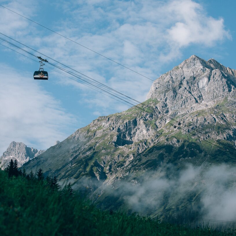 Seilbahn gleitet vor majestätischem Berg und blauem Himmel.