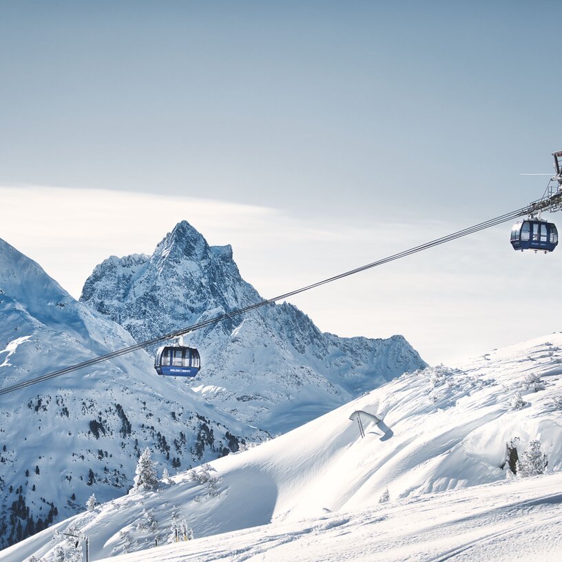 Berglandschaft mit Seilbahn und schneebedeckten Gipfeln unter klarem Himmel.