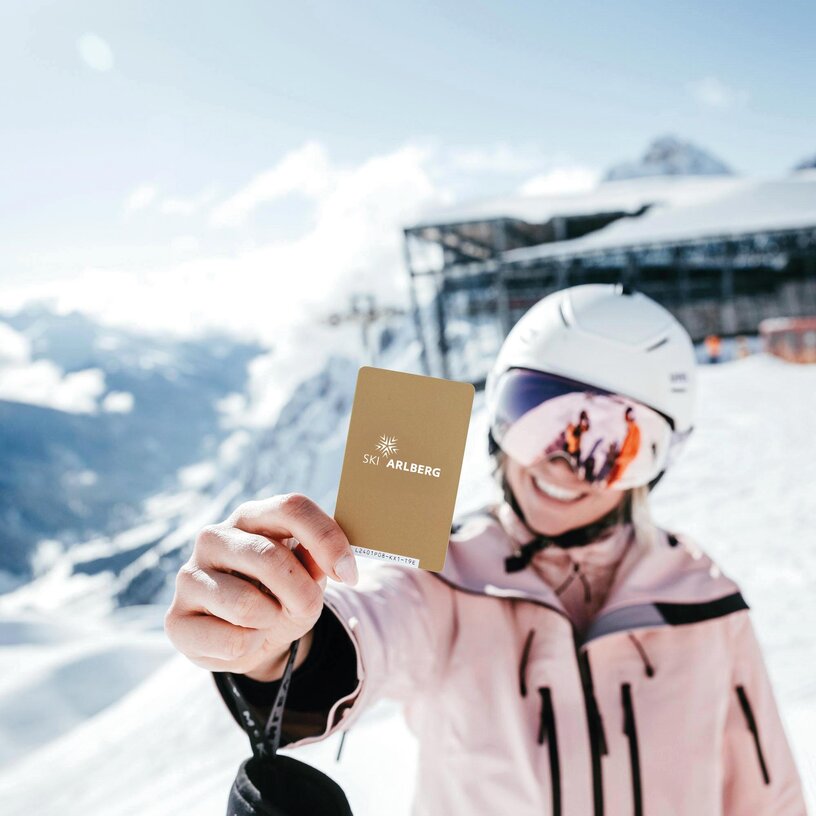 Skifahrerin hält eine goldene Arlberg-Skikarte in der Hand.
