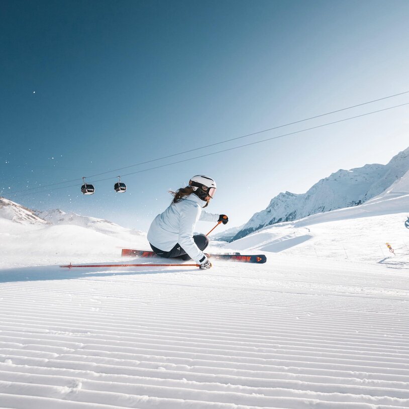 Skifahrerin in Aktion auf einer schneebedeckten Piste bei klarer Sonne.