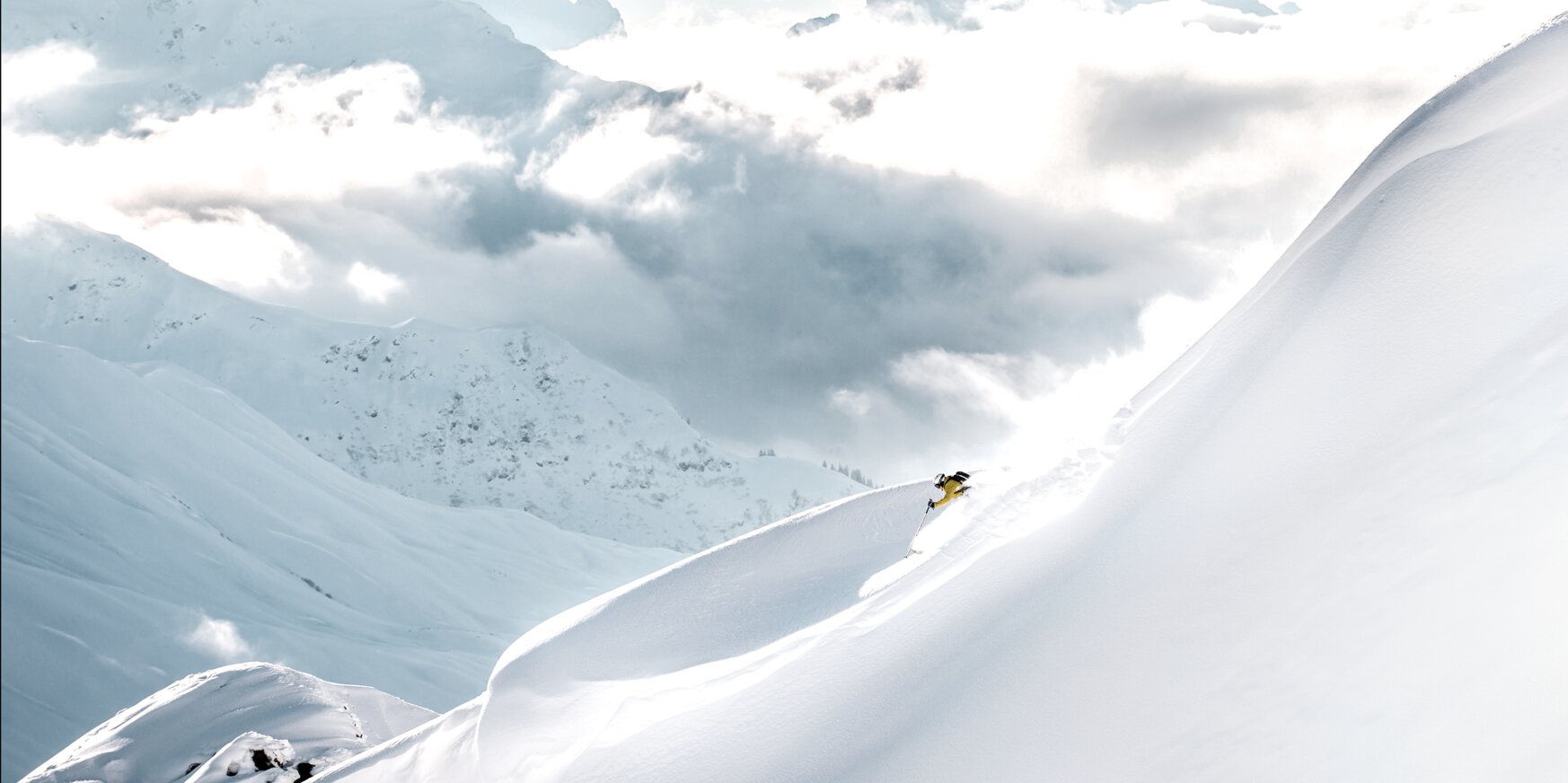 Ein Skifahrer auf einem verschneiten, hohen Berg mit Wolken im Hintergrund.
