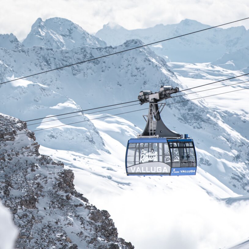 Eine Gondelbahn fährt durch eine winterliche Alpenlandschaft.
