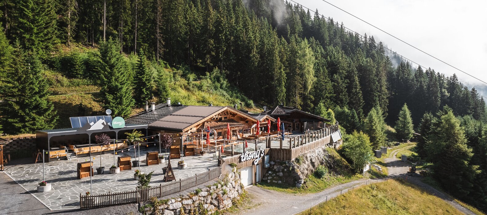 Eine Berghütte inmitten eines Waldes mit Terrasse und Sonnenschirmen.