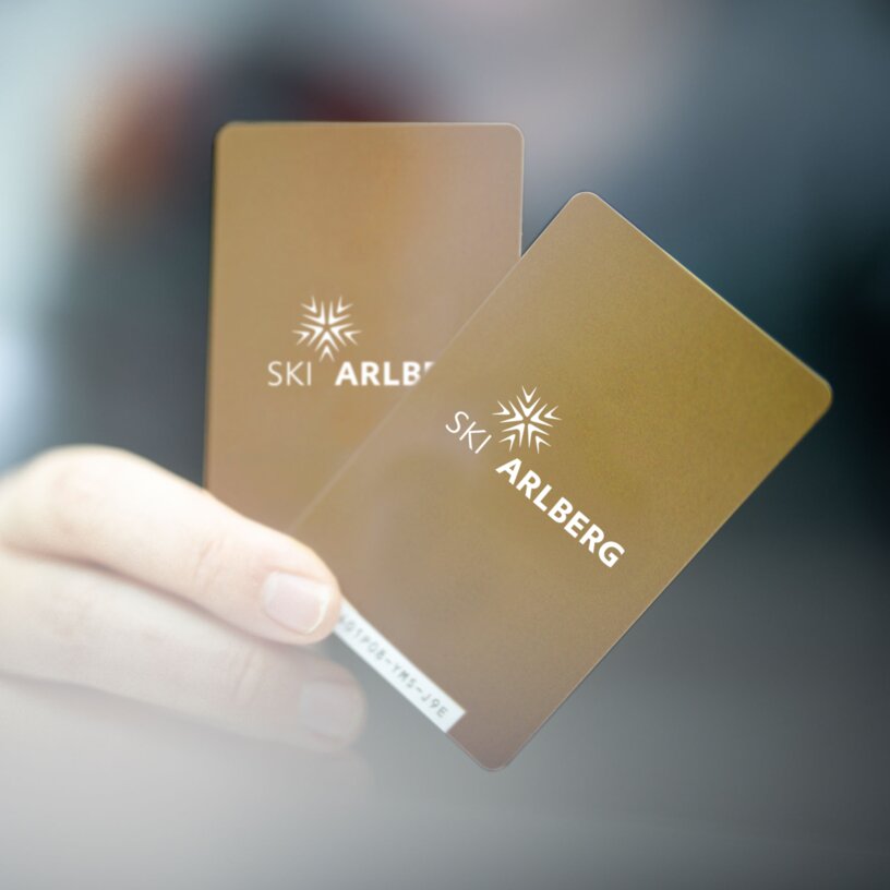 Zwei goldene Skipässe von Ski Arlberg werden von einer Hand gehalten.