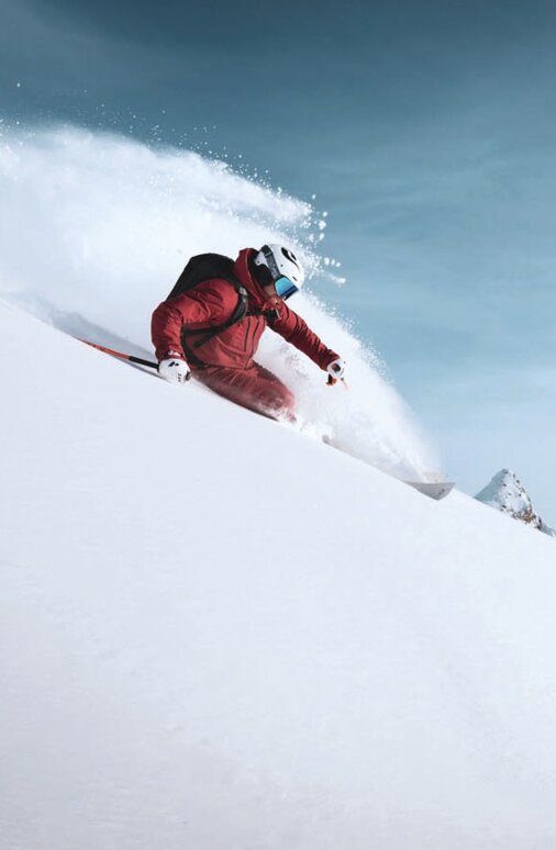 Ein Freerider fährt in rotem Skianzug einen Tiefschnee-Hang in St. Anton am Arlberg hinunter.