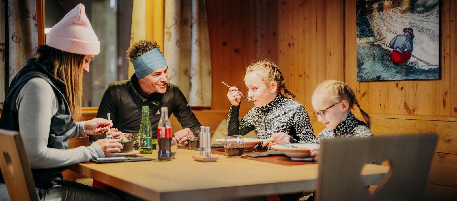 Familie isst zusammen an einem Holztisch in einer Berghütte.