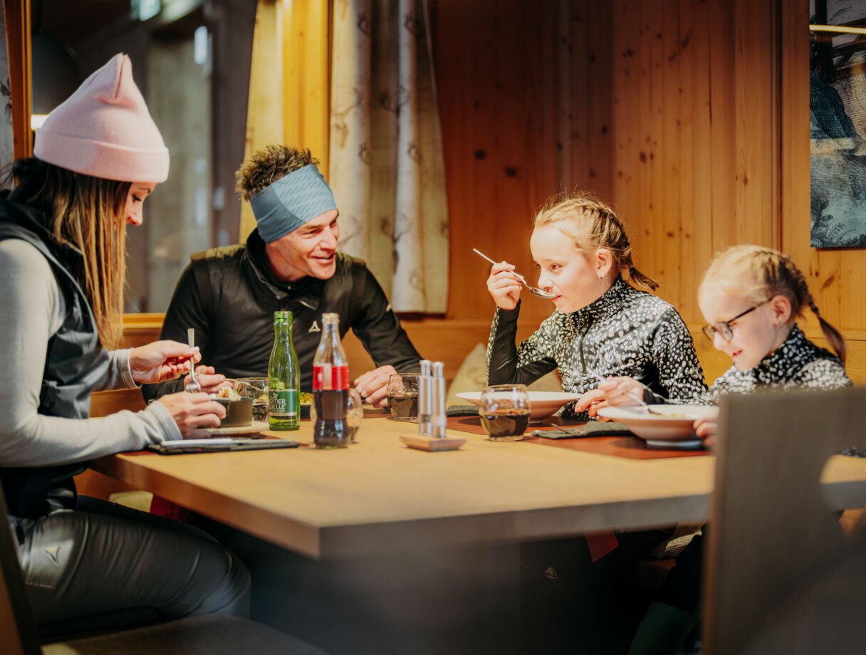 Familie isst zusammen an einem Holztisch in einer Berghütte.