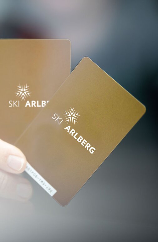 Nahaufnahme zweier goldener Ski Arlberg Skipässe in einer Hand.