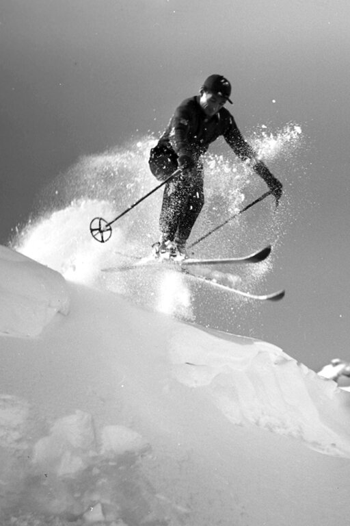 Schwarz-Weiß-Bild  von einem Skifahrer, der über eine Schneeverwehung in springt.