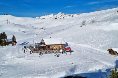 Schneebedeckter Berggasthof Aufelder Hütte umgeben von Skifahrern.