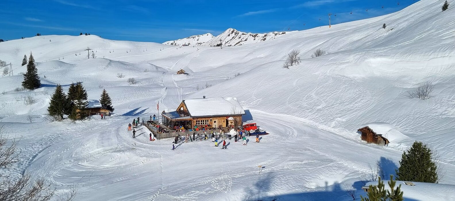 Schneebedeckter Berggasthof Aufelder Hütte umgeben von Skifahrern.