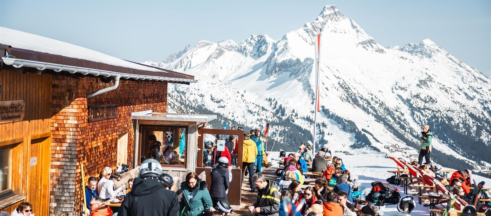 Skifahrer genießen sonnige Terrasse der Punschhütte Wartherhorn.