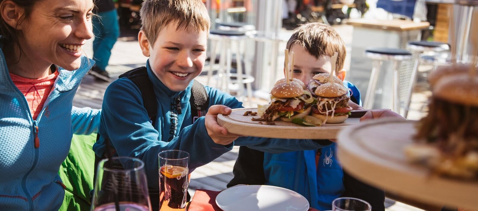 Eine Familie genießt Burger und Getränke in der S1 Skilounge.