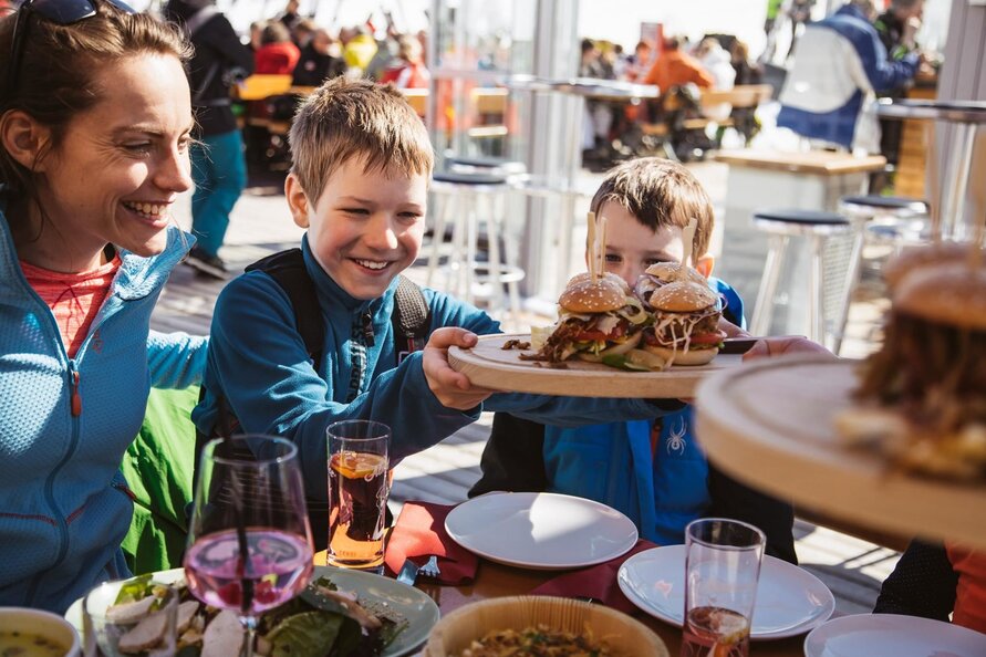 Eine Familie genießt Burger und Getränke in der S1 Skilounge.