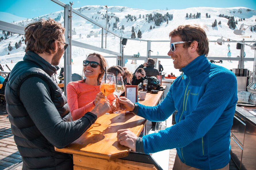 Personen genießen Drinks in der S1 Skilounge mit Bergblick.