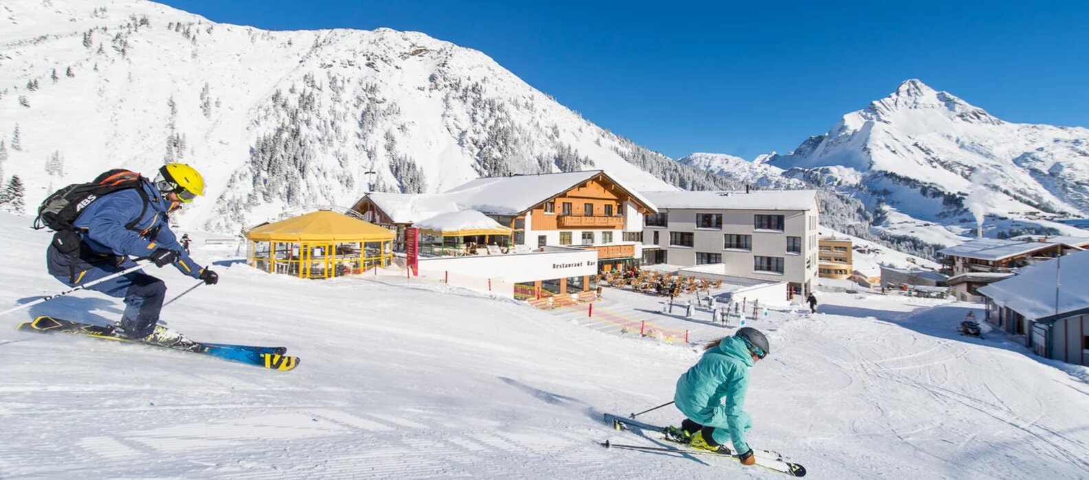 Skifahrer vor der Steffisalp Schirmbar mit verschneiten Bergen im Hintergrund.