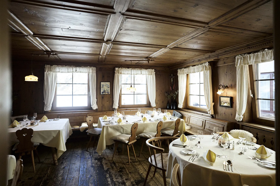 Holzverkleidete Gaststube mit gedeckten Tischen.