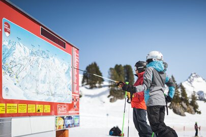 Zwei Skifahrer schauen auf eine Pistenkarte in einem Skigebiet.