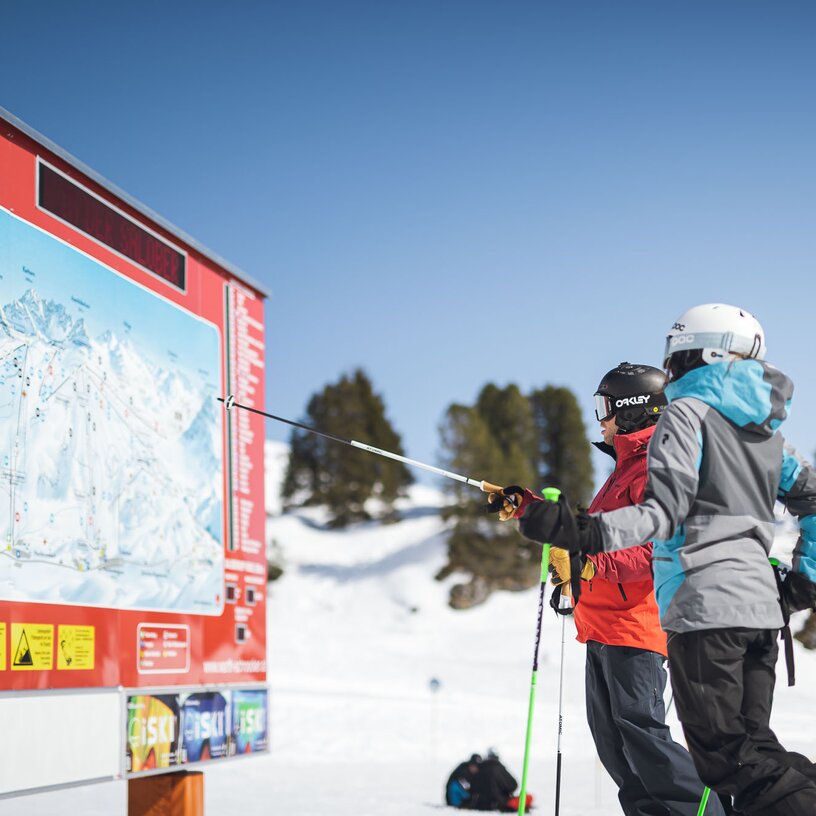 Zwei Skifahrer schauen auf eine Pistenkarte in einem Skigebiet.