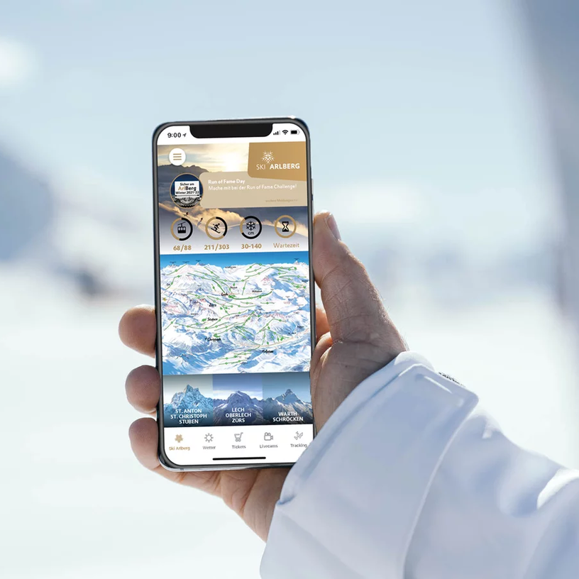 Person hält Smartphone mit Ski-App vor Schneelandschaft.