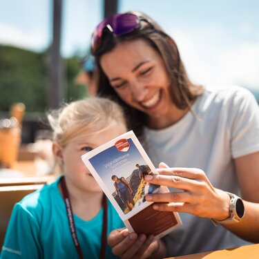 Lächelnde Frau und Kind schauen gemeinsam eine Wanderkarte an.