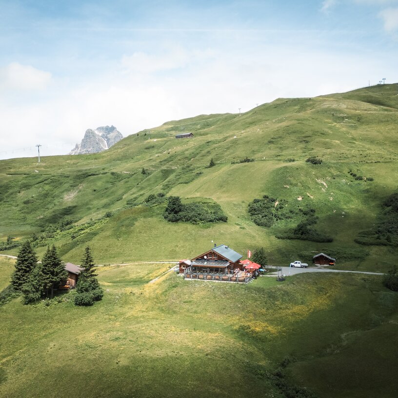 Eine Berghütte auf einem grünen Hügel mit Berg im Hintergrund.