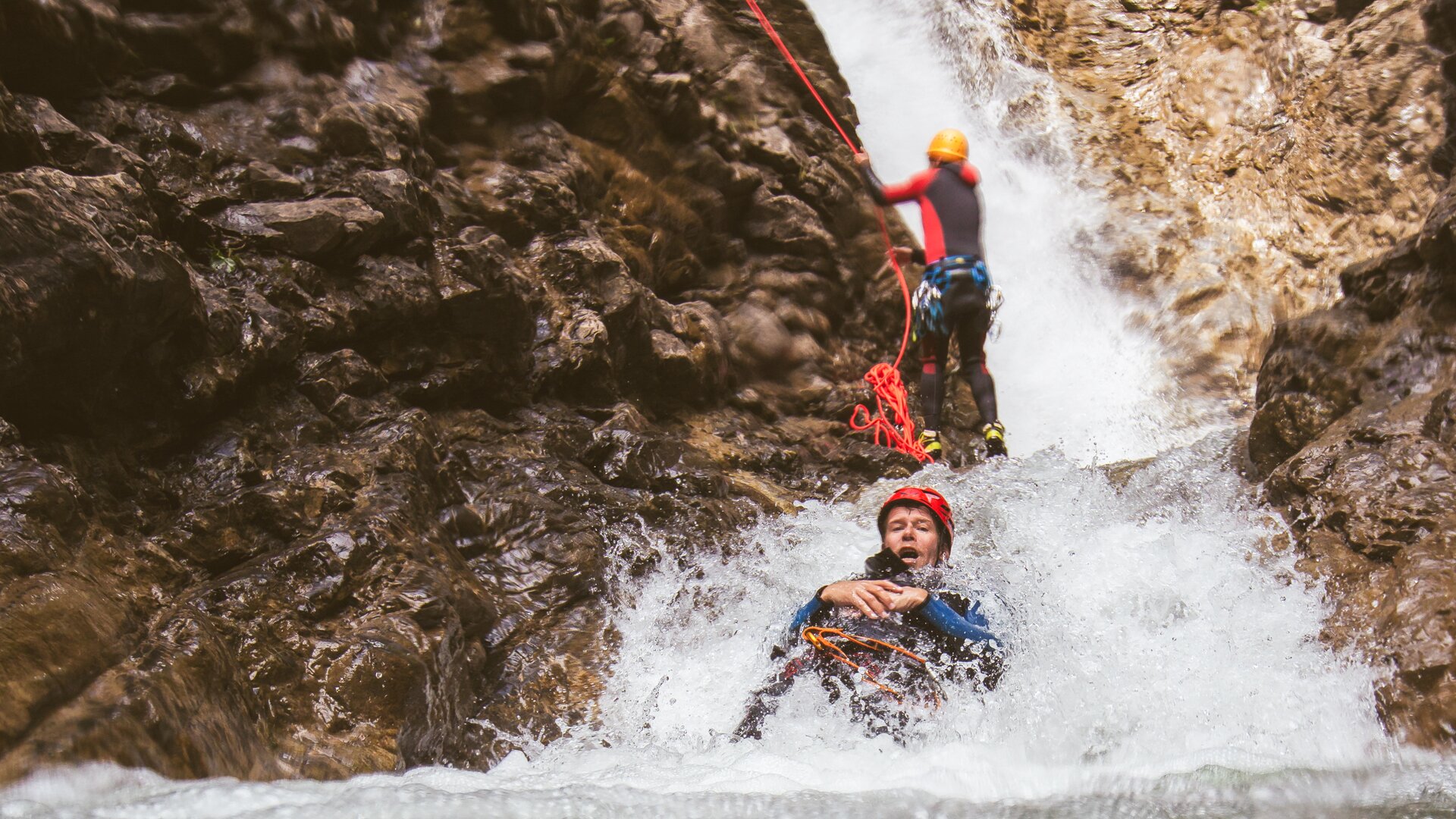 Personen beim Canyoning an einem Wasserfall mit Kletterausrüstung.