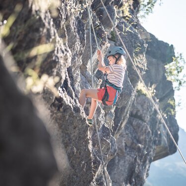 Ein Kind mit Helm und Klettergurt erklimmt eine Felswand.